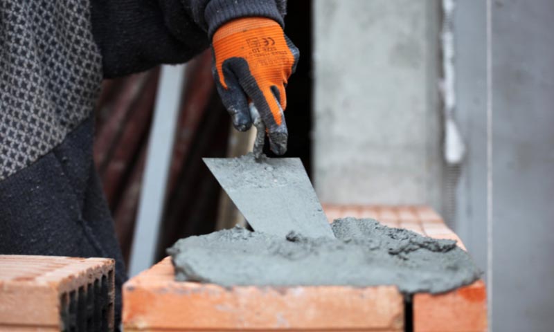 A student applying mortar to a wall of bricks