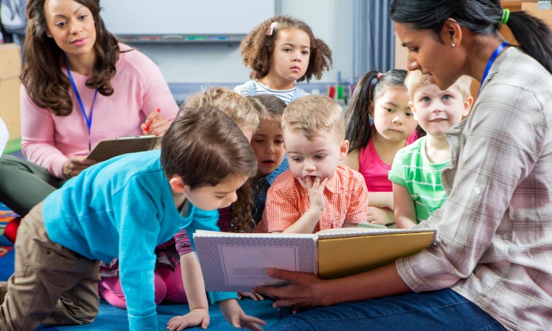 Nursery school teachers showing young children a book