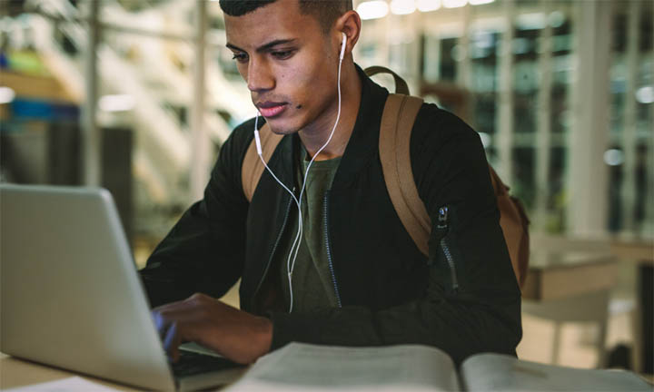 A student studying with earphones in, at a laptop